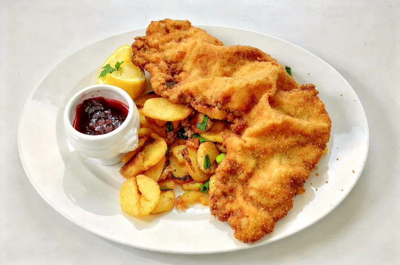 FLUX.2 Max output: the same schnitzel plate on a light grey surface, crumbs left on the plate